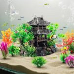 A gray resin castle aquarium decoration with arched entrances, surrounded by eight green and purple artificial aquarium plant
