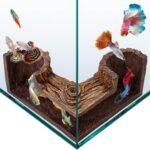 A dark brown, textured FISHNOSH aquarium cave, designed to look like natural driftwood, placed in a fish tank corner.