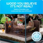 A dark brown, textured FISHNOSH aquarium cave, designed to look like natural driftwood, placed in a fish tank corner.