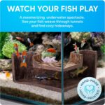A dark brown, textured FISHNOSH aquarium cave, designed to look like natural driftwood, placed in a fish tank corner.
