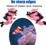 Two pink floating diver ornaments with tiny oxygen tanks and cameras, submerged in a clear fish tank with bubbles.